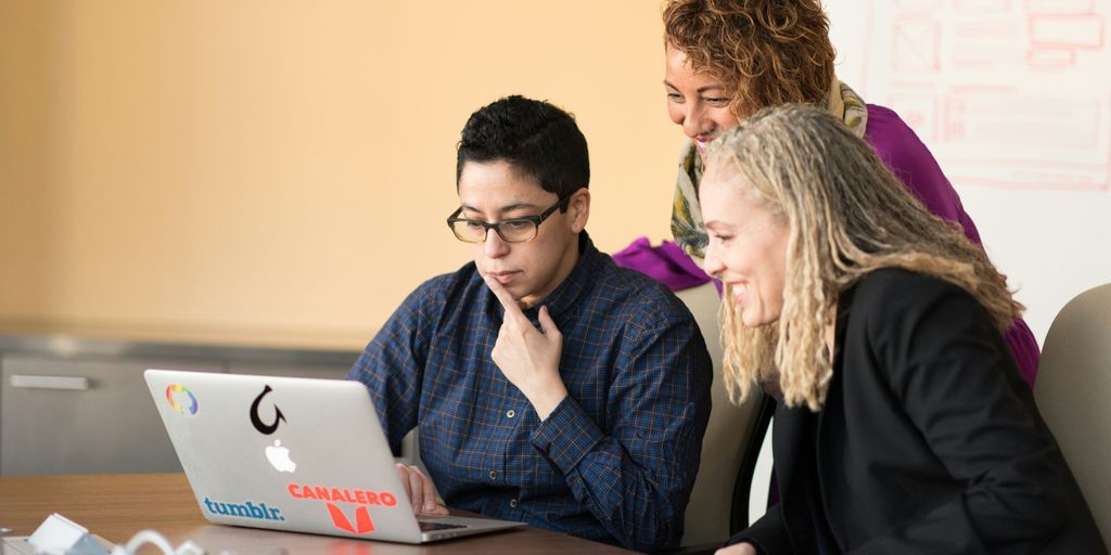 three women beside table looking at MacBook