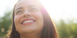 Person smiling, looking up towards sunlight.